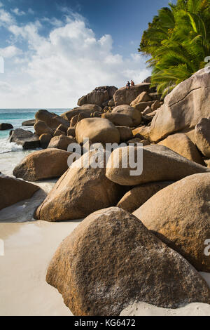 The Seychelles, Praslin, Anse Georgette, beach couple sat on rocks at edge of beach