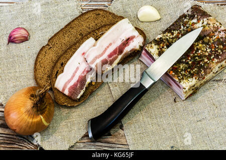 On the table is a slice of bread with two slices of fresh salted rust, a large piece of bacon, garlic and onions Stock Photo