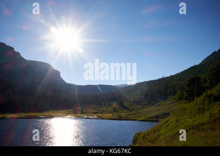 Bright sunburst over a tranquil Colorado mountain lake in the Flat Tops Wilderness with the sun casting a glowing path over the surface of the water Stock Photo