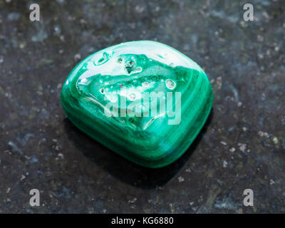 macro shooting of natural mineral rock specimen - polished Malachite gemstone on dark granite background Stock Photo