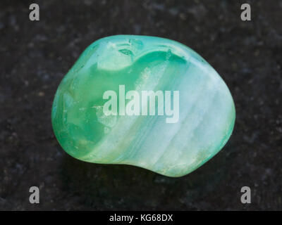 macro shooting of natural mineral rock specimen - tumbled green dyed agate gemstone on dark granite background Stock Photo