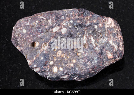 macro shooting of natural mineral rock specimen - pebble of porous basalt stone on dark granite background from Buryatia, Russia Stock Photo