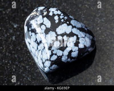 macro shooting of natural mineral rock specimen - tumbled snowflake obsidian gem stone on dark granite background from USA Stock Photo