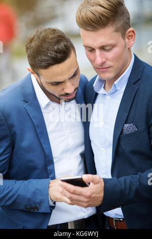 two handsome young businessmen standing outside and looking at phone Stock Photo