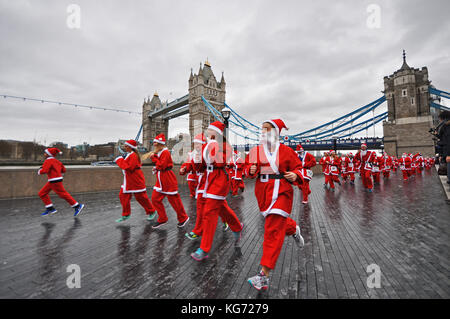 Santa in the City charity fun run London. Passing Tower Bridge. Santas in Santa suits running. Santa dash Stock Photo