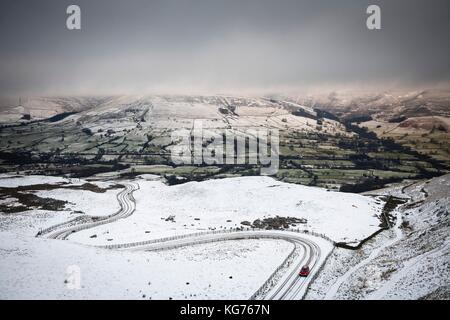 A car drives up a snow covered mountain road in winter. Edale valley, Peak District, UK Stock Photo