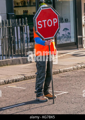 Road Worker standing in road holding Stop sign, London Stock Photo