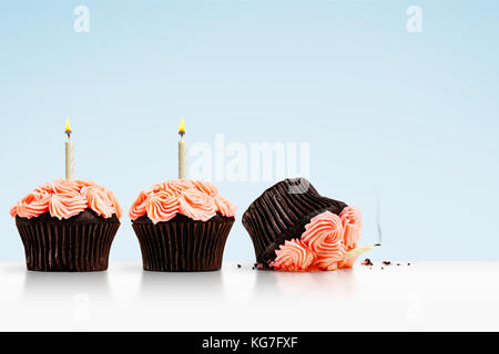 Smashed cupcake in row of cupcakes with candles on blue background Stock Photo