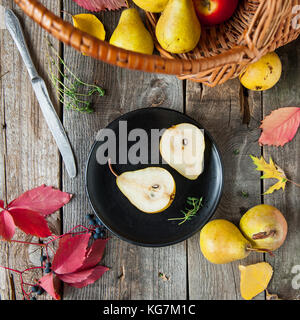 Autumn harvest concept - cut fresh ripe pear on the black plate and group of yellow pears in the basket and on the rustic wooden table, Vegetarian, ve Stock Photo