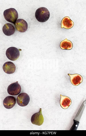 Whole and halved figs and a knife on a white marbled background with lots of copy space. Top view. Stock Photo