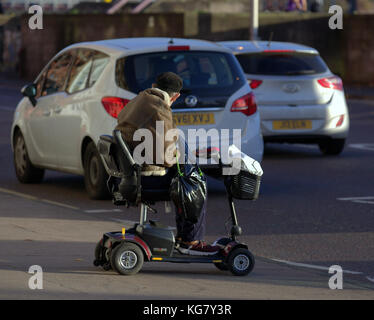 old man on electric mobility scooter waiting to cross busy road viewed from behind Stock Photo