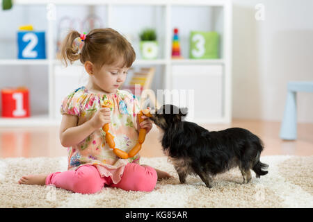 Little girl feeds dog on floor in room