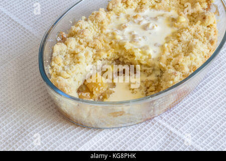 Cooked apple crumble pie in glass oval dish on white cloth Stock Photo