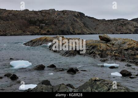 Looking from the beach across the water to the far side of the bay, Brigus, Newfoundland and Labrador, Canada. Rocky coastline, some ice in bay. Stock Photo