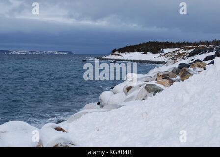 Snow and Ice covered coastline, looking across the bay to Bell Island, under gathering storm cloud. Conception Bay South, Newfoundland.
