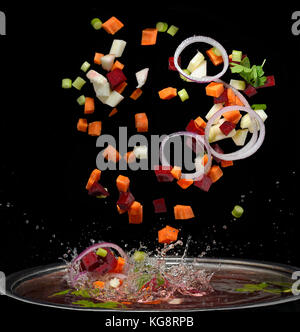 Cut vegetables splash in water soup cooking concept isolated on black background Stock Photo