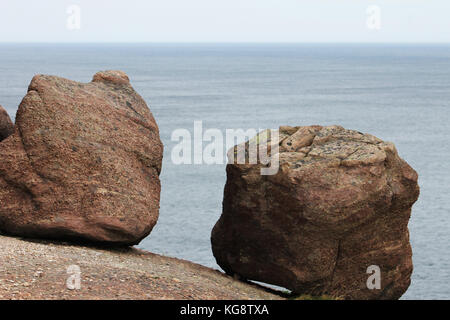 Two large boulders resting on the edge of the cliff, against a background of blue water and blue sky, Signal Hill, Newfoundland.. Stock Photo