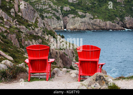 Looking out from behind two red Adirondack chairs anchored to the cliff side, overlooking the bay. Signal Hill trails, St. John's, Newfoundland. Stock Photo