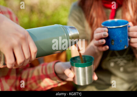 Two women enjoying hot coffee on a hike pouring it from a thermal flask into mugs in a close up view of their hands Stock Photo