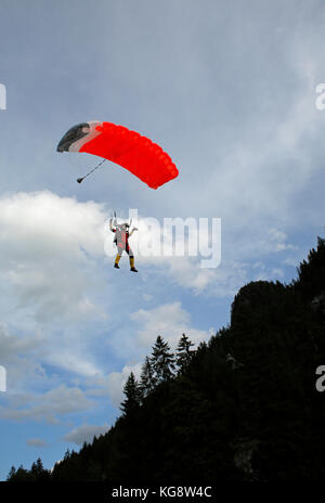 Skydiver under canopy is flying in the sky and approaching the landing area. Soon the jumper is stepping down and walking save away. Stock Photo