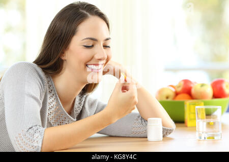 Happy woman taking omega 3 vitamin pills on a table at home with a colorful background Stock Photo