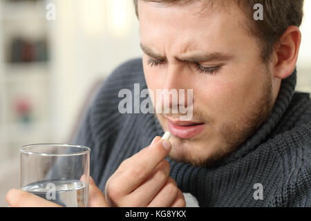 Ill man wearing jersey, sweater, jersey, taking a pill in winter sitting on a sofa in the living room in a house interior Stock Photo
