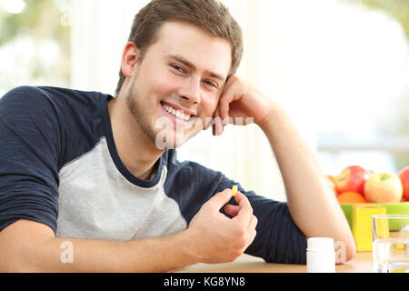 Happy man holding omega 3 vitamin pill on a table at home with a colorful background Stock Photo