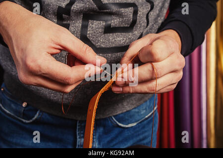 A close-up of a weed man in a T-shirt and jeans makes a genuine leather strap, makes holes for a buckle for buckles, in background is natural leather Stock Photo