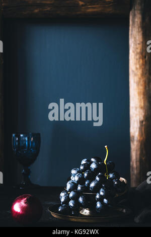 Still life of black grapes on vintage tray over blue background. Vertical, retro style, copy space for text Stock Photo