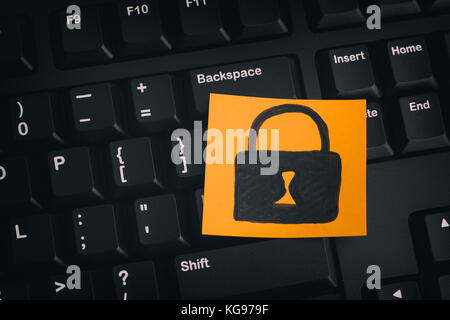 Data Security Concept. Yellow paper note with closed padlock on a black keyboard. Close up. Stock Photo