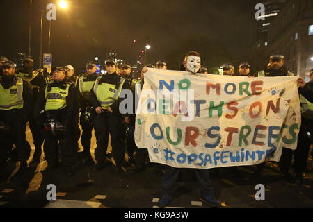 A protester holds a banner in front of police in Trafalgar Square, London, during the Million Mask March bonfire night protest organised by activist group Anonymous. Stock Photo