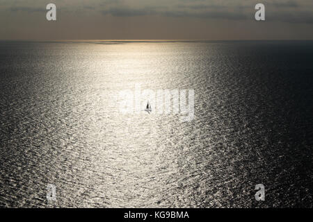 Solitary sailing boat or yacht caught in the sun's reflections on a wide expanse of sea Stock Photo