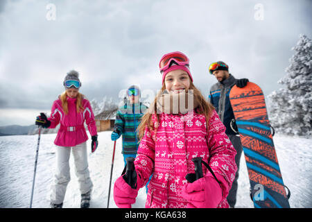 young smiling girl with family on ski slope on vacation in mountain together Stock Photo