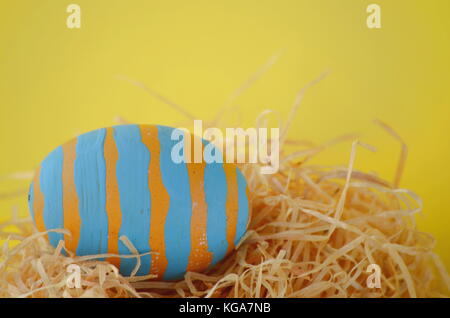 Hand painted aqua blue striped Easter egg in a nest on a bright yellow background with copy space. Stock Photo