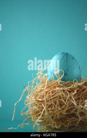 Hand painted aqua blue Easter egg with blue glitter in a nest on a turquoise teal blue green background with copy space. Stock Photo