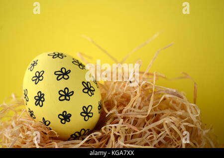 Hand painted yellow Easter egg with black flowers in a nest on a bright yellow background with copy space. Stock Photo