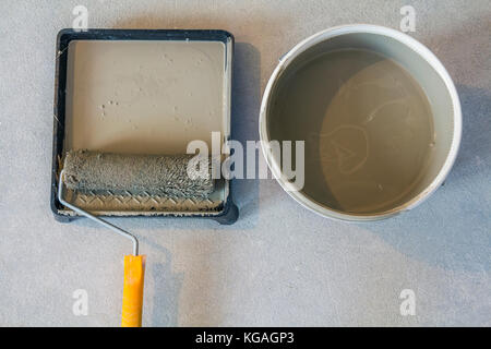 High angle of paint roller in tray with paint can on concrete floor. Stock Photo