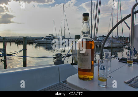 Sonderborg, Denmark - June 30th, 2012 - Bottle of single malt whisky with glasses on the table in the cockpit of a sailing yacht with a marina in the 