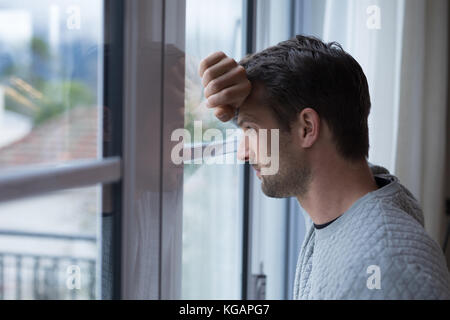 Thoughtful man looking through window at home Stock Photo