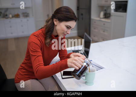 Beautiful woman pouring black coffee in mug at desk Stock Photo