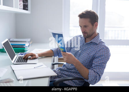 Man looking at graph while using laptop at desk Stock Photo