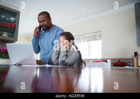 Father talking on mobile phone and daughter watching in kitchen Stock Photo