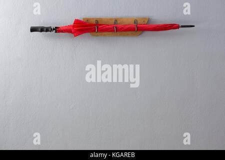 Red umbrella kept on hook against wall Stock Photo