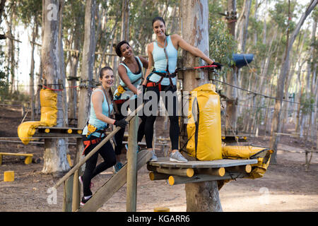 Portrait of happy friends preparing for zip line in forest on a sunny day Stock Photo