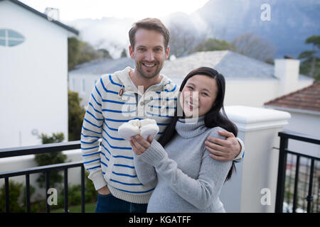 Pregnant woman and her husband holding baby socks in balcony at home Stock Photo