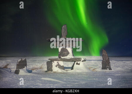 A symbol of the Canadian north, a stone inukshuk sits in the snow with the aurora borealis in the background. It means  'you are on the right path.' Stock Photo