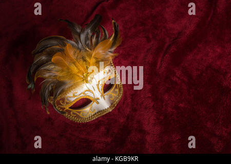 Brown golden venetian carnival mask with feathers seen from above on a draped red velvet theater curtain Stock Photo