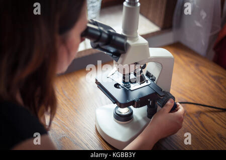 Woman looking through microscope at home Stock Photo