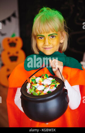 Girl in pumpkin costume holding a bowl full of candies Stock Photo