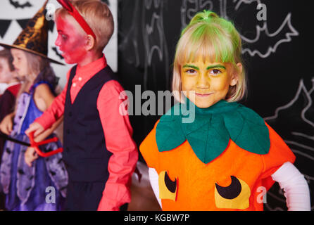 Cute girl in pumpkin costume celebrating halloween with friends Stock Photo